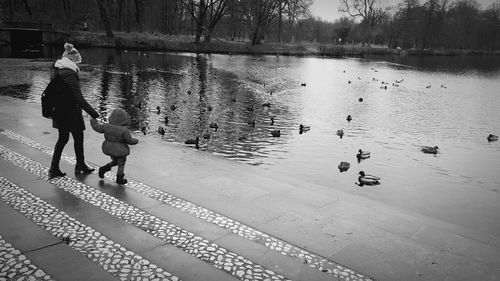 Mother with daughter looking at ducks swimming in lake at public park