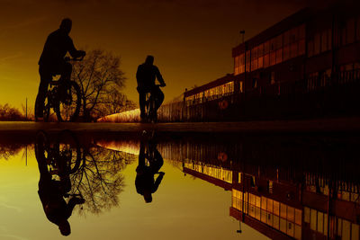 Silhouette people on lake against sky during sunset