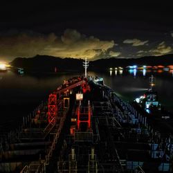 Illuminated pier over river against sky at night