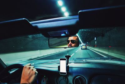 Reflection of man in rear-view mirror of car on road
