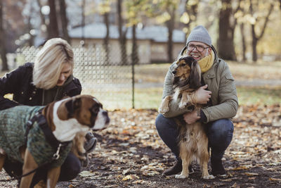 Smiling man crouching while embracing pet and looking at woman with boxer dog