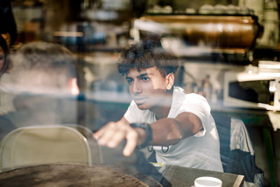 Teenage boy consoling his friend while sitting at cafe seen through glass window