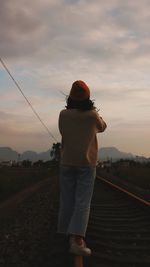 Rear view of woman standing on railroad track during sunset