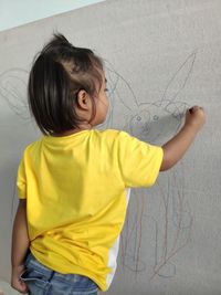 Rear view of girl looking away against yellow wall