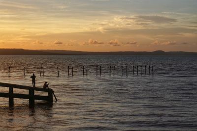 Silhouette man sitting on beach against sky during sunset