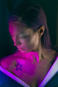 Close-up of mid adult woman with star shape tattoo against black background