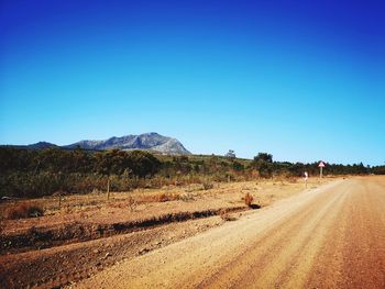 Dirt road on field against clear blue sky