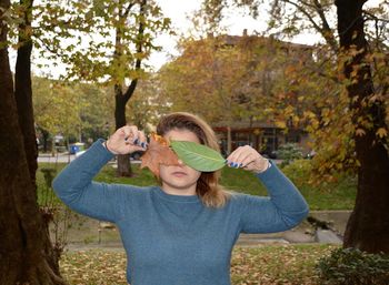 Young woman covering eyes with leaves in park during autumn