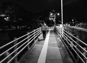 Rear view of man walking on illuminated bridge at night