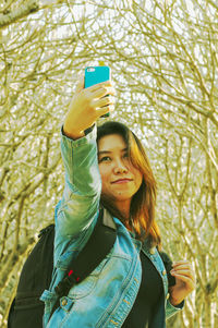 Woman taking selfie from phone while standing against trees
