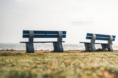 Empty bench on field against sky