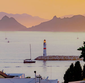 Lighthouse by sea against sky during sunset