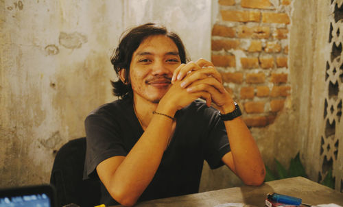 Portrait of young man sitting against wall