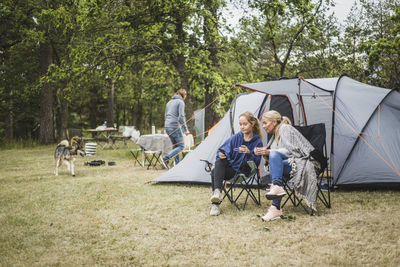 Mother and daughter having coffee while looking at mobile phone in campsite
