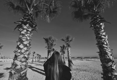 Rear view of woman standing by palm trees against sky