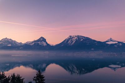 Scenic view of mountains by lake against dramatic sky during sunset