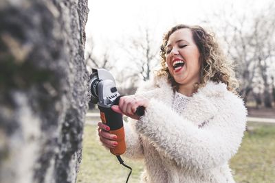 Cheerful woman using hand saw while sawing tree trunk