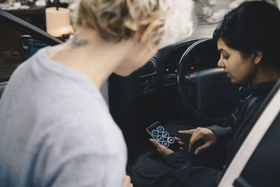 Mechanic explaining application to customer on smart phone while sitting in car