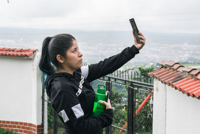 Young latina taking a selfie with her sportswear and a thermos for water in her hand
