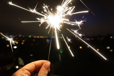 Close-up of hand holding illuminated fireworks against sky at night