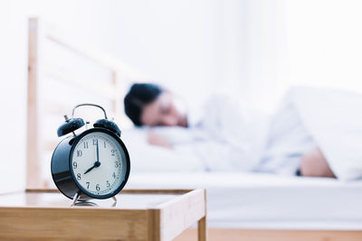 Close-up of alarm clock on side table with woman sleeping in background