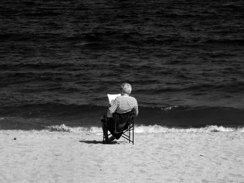 Rear view of woman sitting on chair at beach against sea