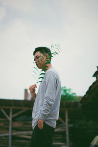 Young man holding leaf while standing outdoors