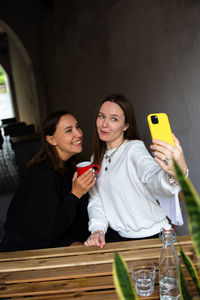 Two women friends have fun outdoors in cafe and take a selfie on a smartphone