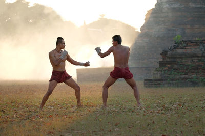 Full length of shirtless men boxing on land against sky