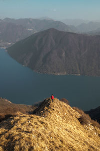 Rear view of man standing on mountain ridge looking at lake