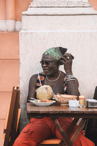 Cool mature african american male in sunglasses and bracelets sitting at urban cafeteria table with coconut beverage