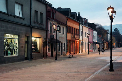 Street lights on sidewalk by buildings in city at dusk