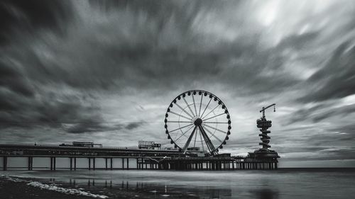 Ferris wheel by sea against sky at dusk