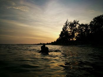 Silhouette man in sea against sky during sunset