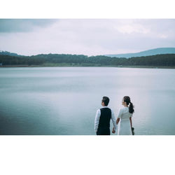 Rear view of friends standing by lake against sky