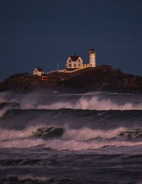 Lighthouse by sea and buildings against sky