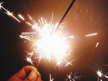 Cropped hand of person holding lit sparklers against wall