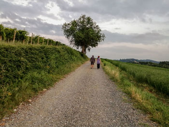 Rear view of two people on road amidst field against sky