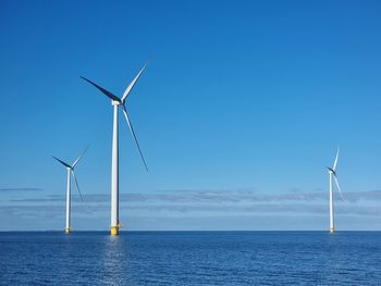 Wind turbines by sea against blue sky