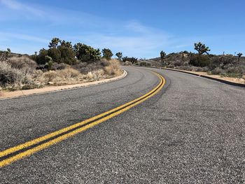 Empty road by trees against sky