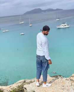 Full length of young man standing on rock in sea