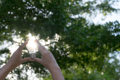 Low angle view of woman hand against trees