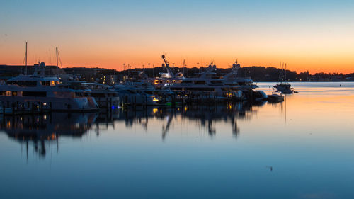 Sailboats moored at harbor against sky during sunset