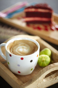 Close-up of coffee cup and figs in serving tray with red velvet cheesecake slice in background
