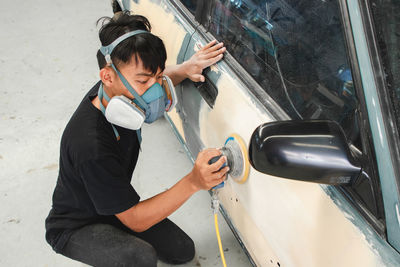 High angle view of boy holding camera while standing by car