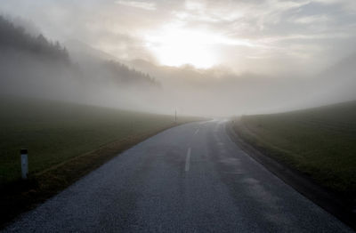 Road amidst landscape against sky during foggy weather