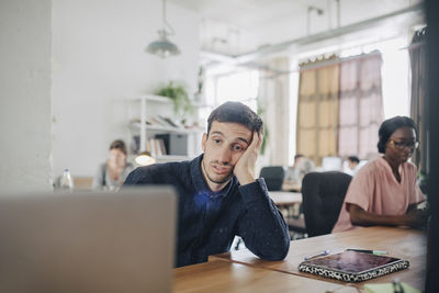 Tired businessman looking at laptop while sitting at desk in creative office