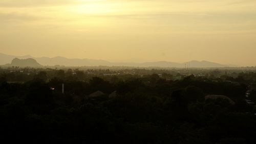 Silhouette trees and cityscape against sky during sunset