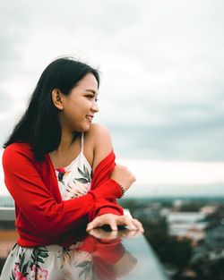 Young woman looking away while standing against sky