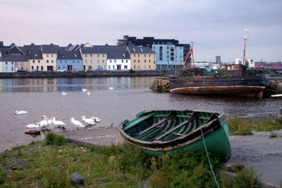 Boats moored on river by buildings in city against sky